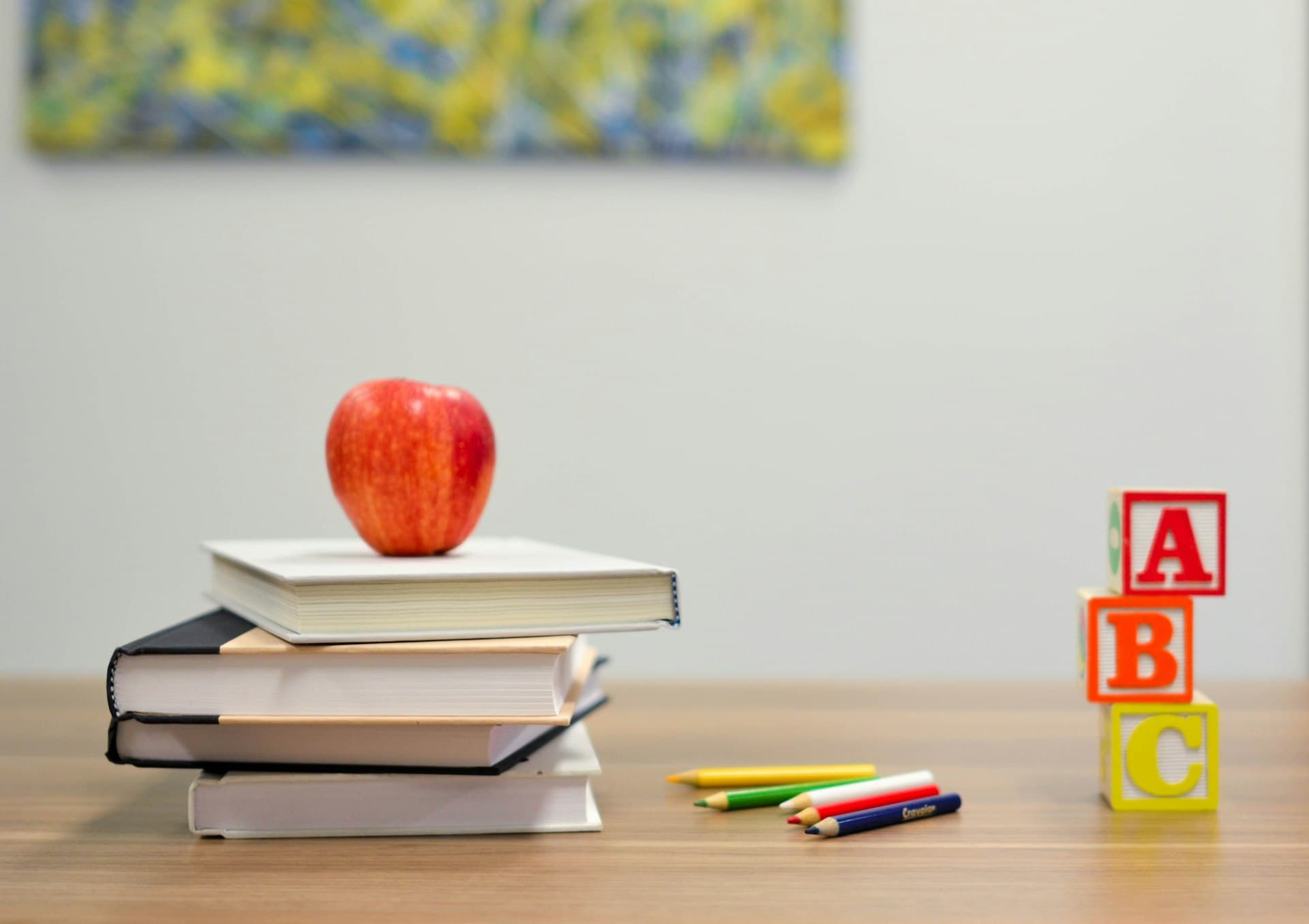 An apple on a stack of textbooks beside coloured pencils and ABC blocks